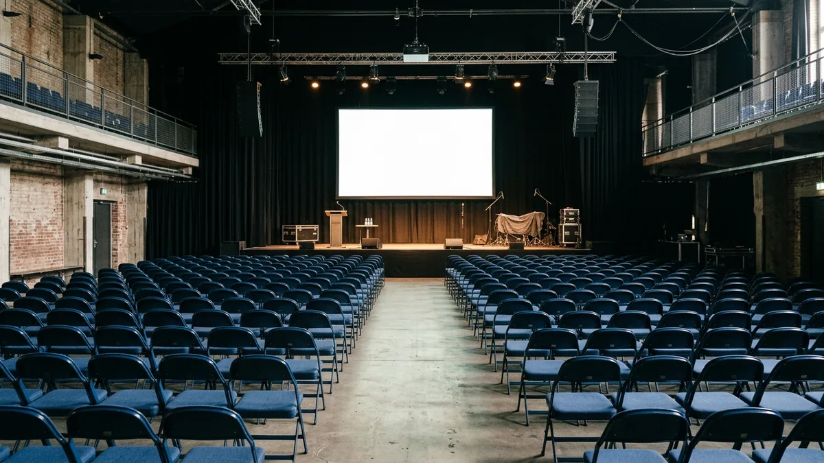 Leerer bestuhlter Saal mit kleiner Bühne und heller Projektionsfläche vor Veranstaltungsbeginn