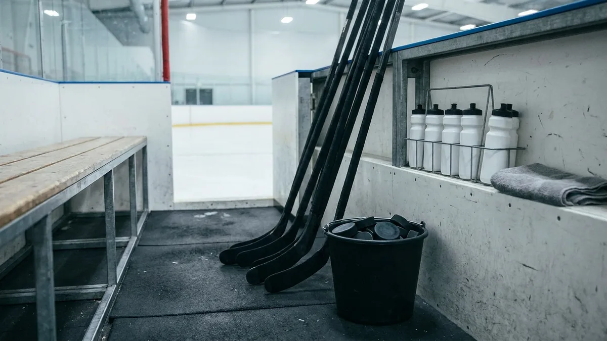 Eishockeyschläger, Puckeimer und Trinkflaschen auf der Spielerbank