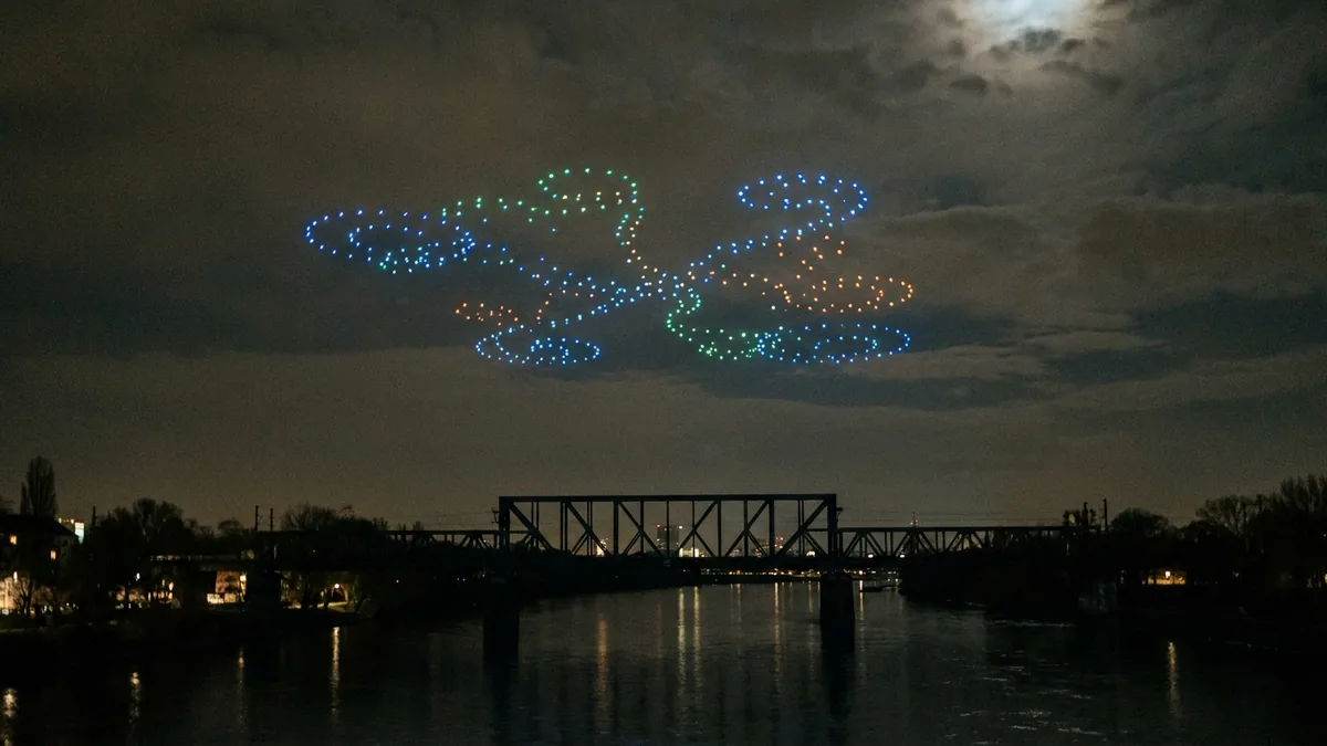 Leuchtender Drohnenschwarm hoch über einem breiten Fluss bei Nacht